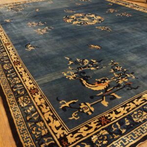 Large dusty blue rug with scattered floral and mythical gold patterns displayed on wood floor.