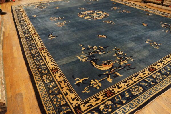 Large dusty blue rug with scattered floral and mythical gold patterns displayed on wood floor.