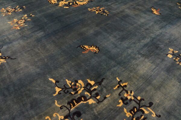 A deep blue rug with striations, detailed with stylized butterflies and flowering branches in gold and black.