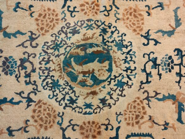 Ornate rug detail featuring a teal and brown circular motif surrounded by floral designs on a beige pile.