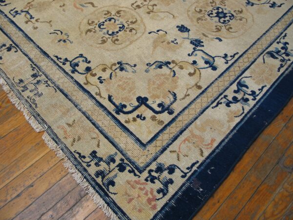 Low-pile rug with a beige ground, detailed blue and tan floral motifs, resting on hardwood floors.
