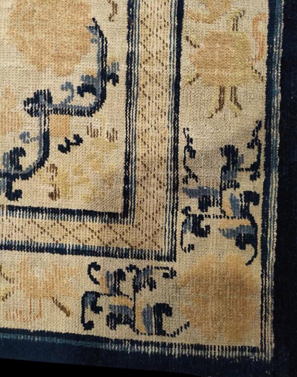 Detailed view of a low-pile rug with a beige field, gold motifs, and a patterned dark blue border.