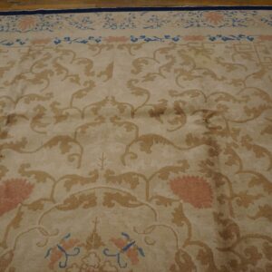 Beige floral rug featuring gold scrolls and pink blossoms, bordered in navy blue, on wood floor.