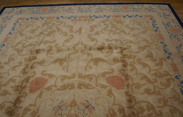 Beige floral rug featuring gold scrolls and pink blossoms, bordered in navy blue, on wood floor.