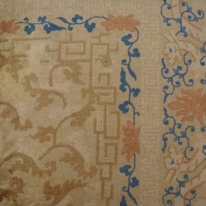 Beige low-pile rug detail showing tan geometric borders and blue/peach scrolling florals next to wood flooring.