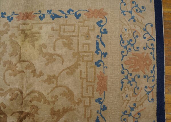 Beige low-pile rug detail showing tan geometric borders and blue/peach scrolling florals next to wood flooring.