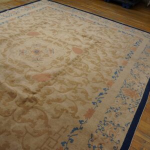 Plush beige rug with tan, pink, and blue designs bordered in navy rests on plank wood flooring.