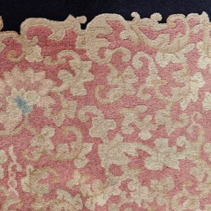 Textured high-pile rug with sprawling tan and pink floral motifs meeting a dark blue border.