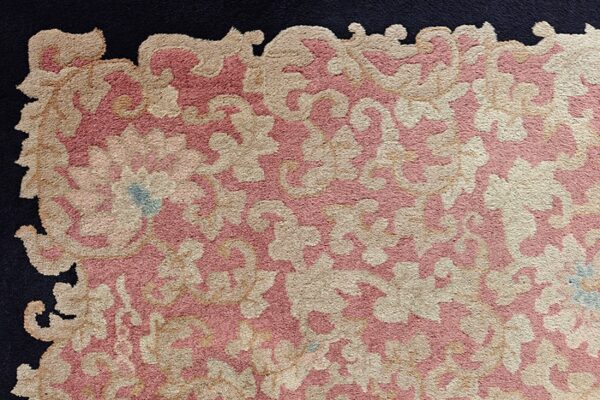 Textured high-pile rug with sprawling tan and pink floral motifs meeting a dark blue border.