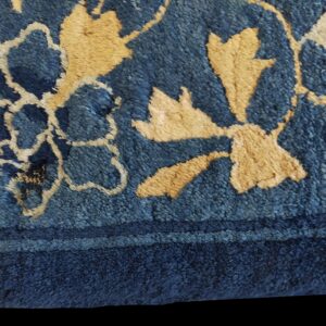 Extreme close-up of a textured high-pile rug showing dark blue and tan floral motifs near a solid border.