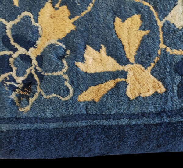 Extreme close-up of a textured high-pile rug showing dark blue and tan floral motifs near a solid border.