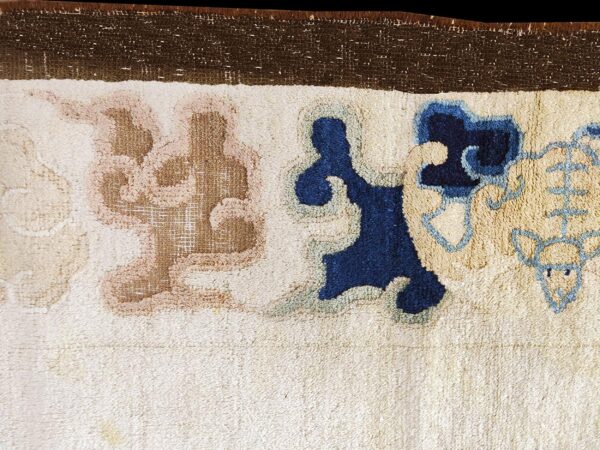 A cream rug border features thick pile and stylized shapes in navy blue, light blue, and dusty tan.