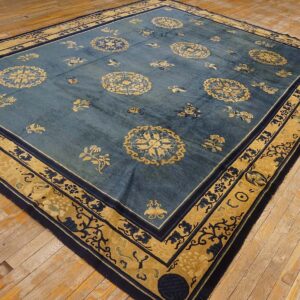 Low-pile blue rug with gold and navy botanical patterns resting on rustic hardwood flooring.