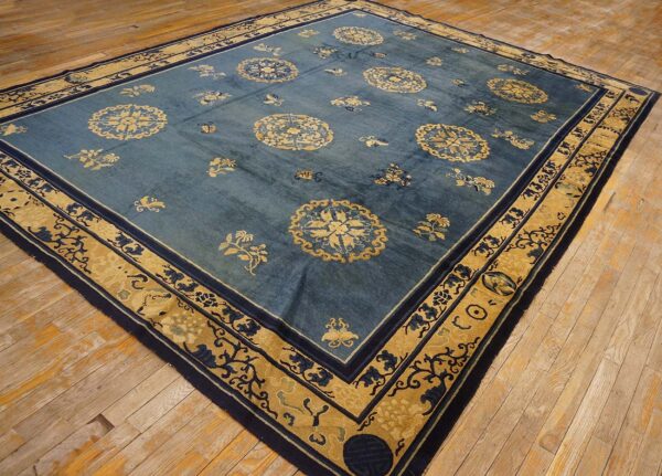 Low-pile blue rug with gold and navy botanical patterns resting on rustic hardwood flooring.