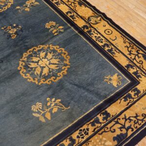 Low pile rug in blue and gold with elaborate floral patterns rests on blonde hardwood floor.