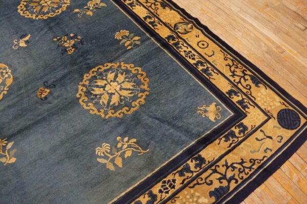 Low pile rug in blue and gold with elaborate floral patterns rests on blonde hardwood floor.