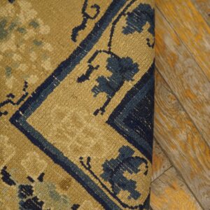 Tan and navy patterned rug with low pile detail rests beside rustic wood flooring with yellow accents.