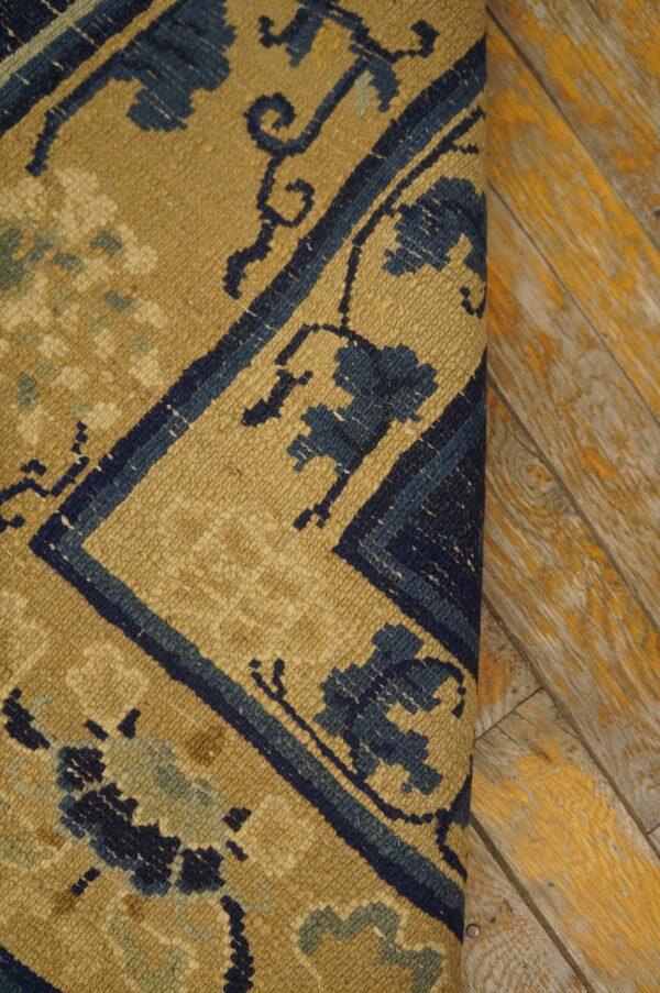 Tan and navy patterned rug with low pile detail rests beside rustic wood flooring with yellow accents.