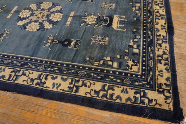 A traditional indigo and tan rug featuring ornate motif borders rests on hardwood planks.