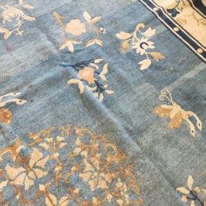 Distressed blue pile rug featuring light beige floral and butterfly motifs and a wide cream and navy border.