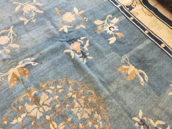 Distressed blue pile rug featuring light beige floral and butterfly motifs and a wide cream and navy border.