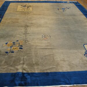 Muted grey rug with visible sheen, wide royal blue border, and scattered floral motifs on a hardwood floor.