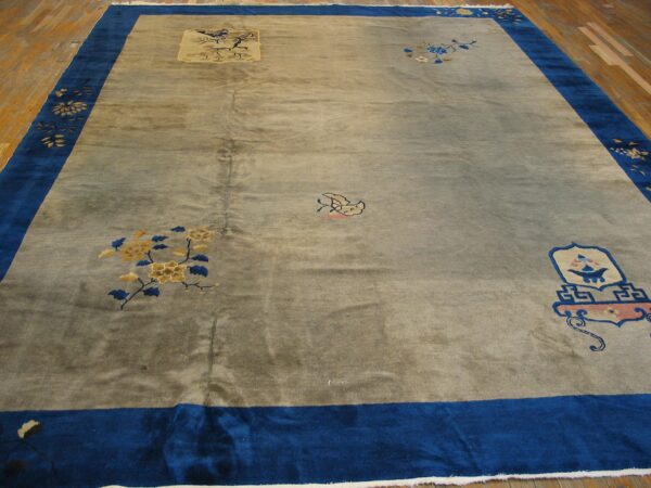 Muted grey rug with visible sheen, wide royal blue border, and scattered floral motifs on a hardwood floor.