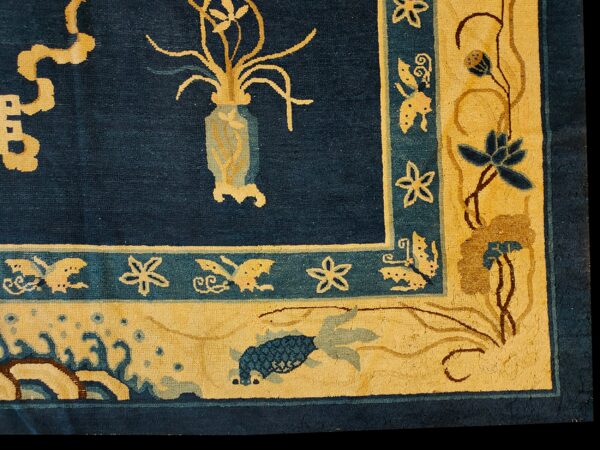 Navy blue rug corner detail shows golden floral, fish, and butterfly patterns on a wide gold border.