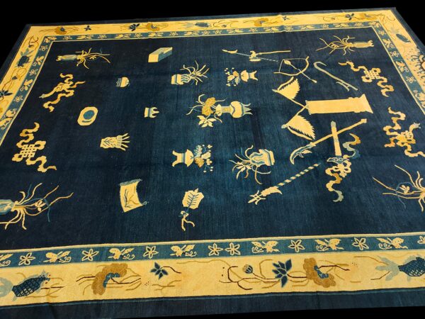 Low pile navy blue rug with gold and teal borders framing scattered symbolic object motifs.