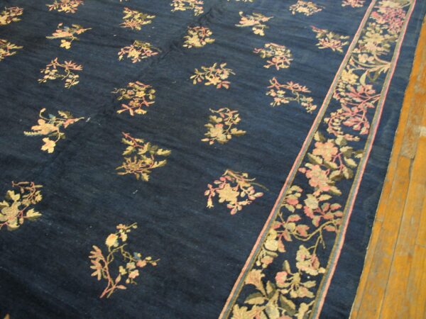 Deep blue rug featuring scattered pink and cream florals, a wide border, and visible wood plank flooring.