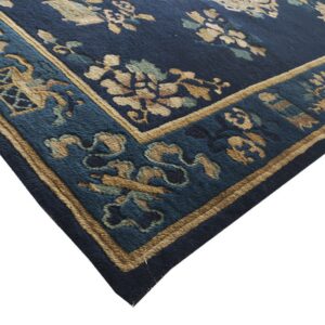 Close up of a dark blue rug corner featuring tan and teal botanical patterns and a multi-layered border.