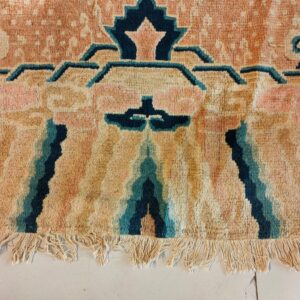 Deep-pile rug in peach, tan, and teal with stylized geometric patterns and visible fringe on tile.