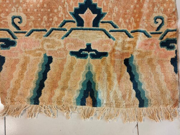 Deep-pile rug in peach, tan, and teal with stylized geometric patterns and visible fringe on tile.