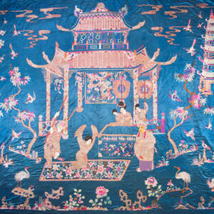 Blue textile with elaborate embroidery depicting pink and gold architecture, people, birds, and flora.