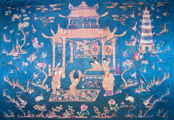 Blue textile with elaborate embroidery depicting pink and gold architecture, people, birds, and flora.