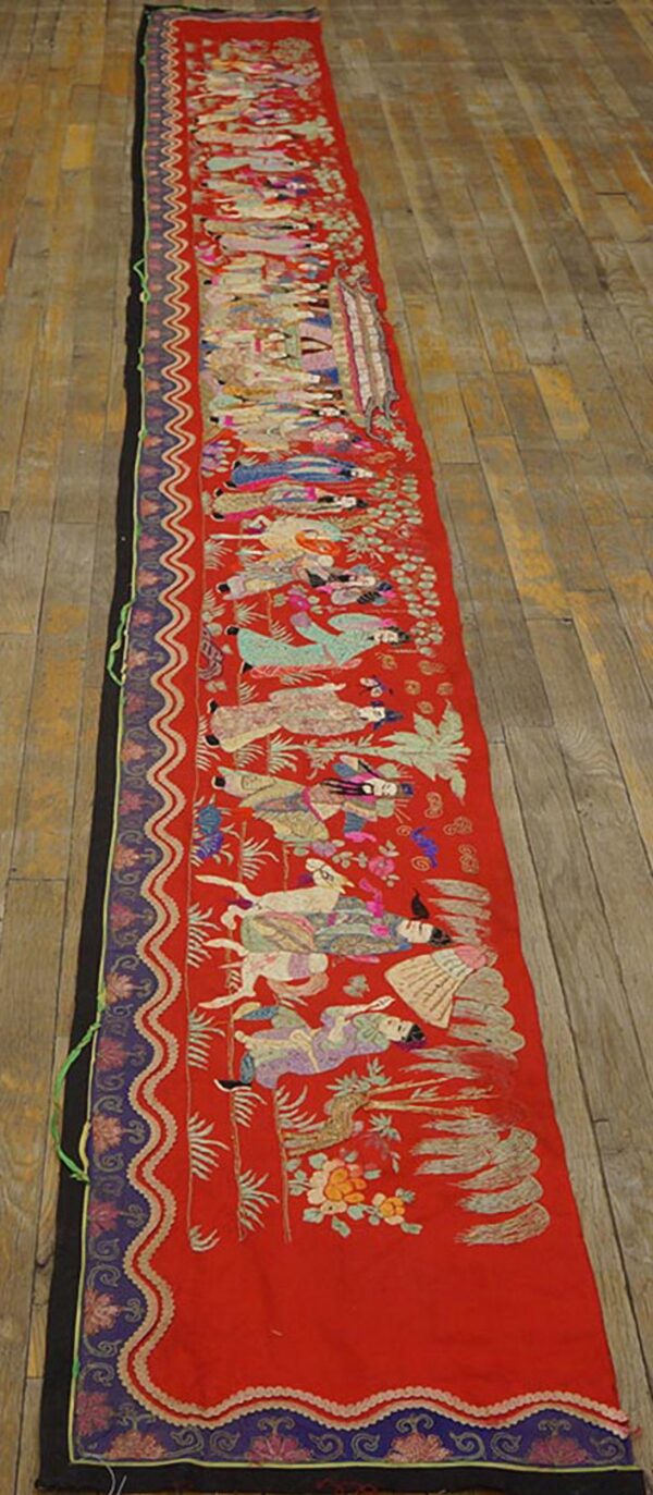 Narrow red runner featuring a multicolor embroidered figural scene and patterned borders on wood flooring.