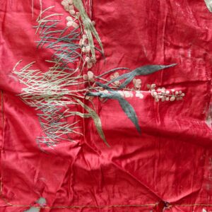 Crumpled red fabric detailed with dense embroidery in sage, charcoal, and blush pink floral motifs.