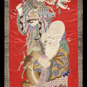 Detailed embroidered red textile with two figures and an animal bordered by a subtle multi-color geometric pattern.