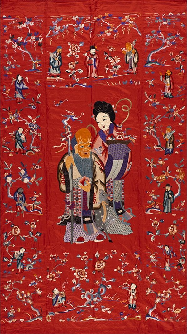 A vertical red embroidered tapestry depicts large and small figures among stylized flowering branches and foliage.