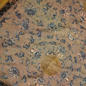 A tan, low-pile rug with a blue and pink floral pattern, featuring a gold central medallion, lying on a wood floor.