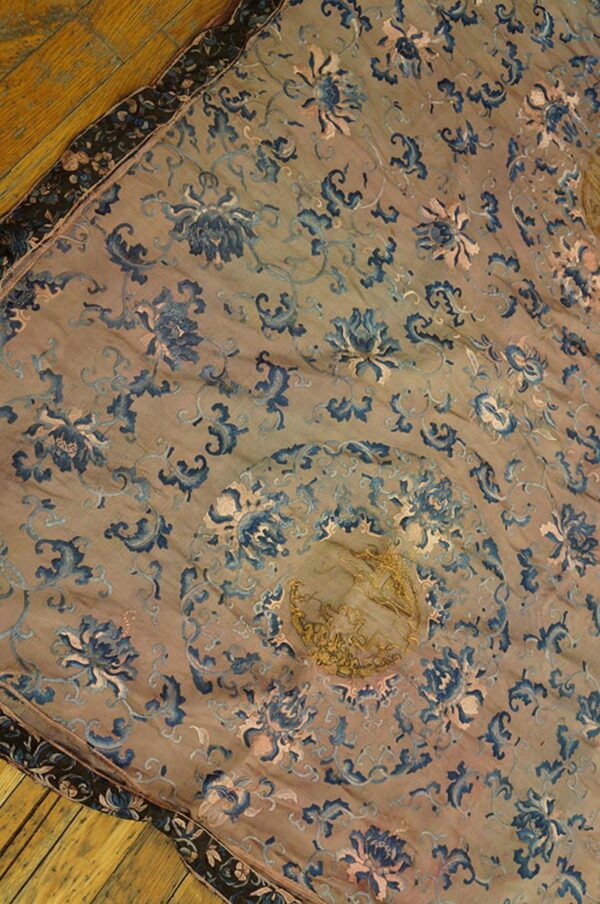 A tan, low-pile rug with a blue and pink floral pattern, featuring a gold central medallion, lying on a wood floor.