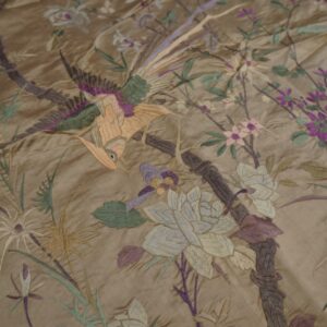 Close-up of a shiny gold textile with embroidered birds, flowers, and foliage in purple, green, and peach.