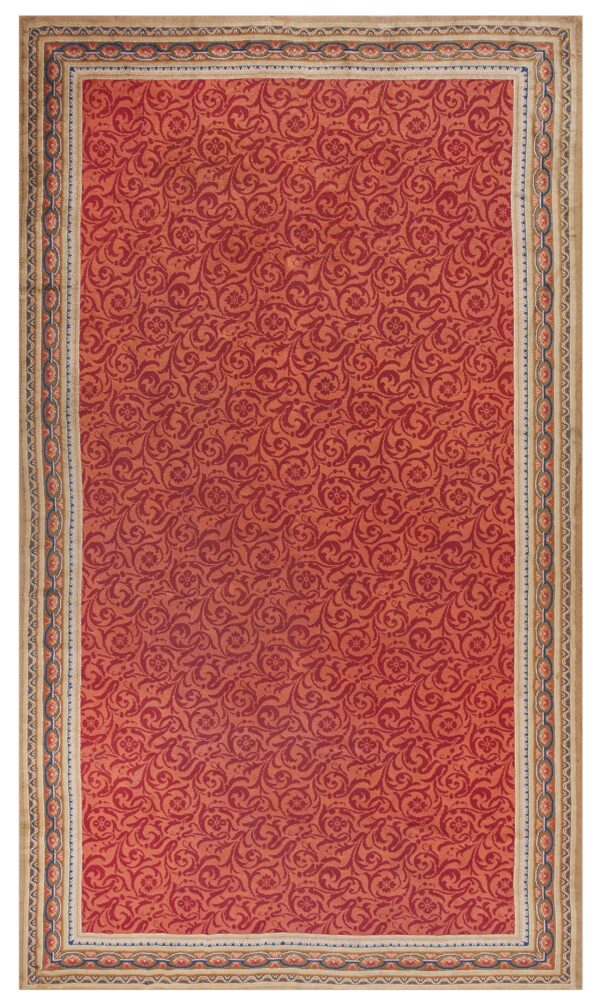 Red rug featuring a scrolling damask pattern and a wide beige border with blue and salmon chain links.