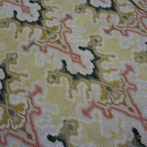 Detail shot of a low-pile textile rug featuring stylized leaves in cream, pale yellow, green, and coral.