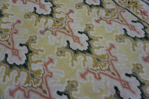 Detail shot of a low-pile textile rug featuring stylized leaves in cream, pale yellow, green, and coral.