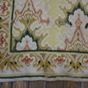 Low-pile rug detail showing yellow, white, green, and orange stylized floral patterns on a wood floor.