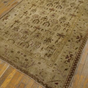 Muted gold traditional rug with brown and purple stylized motifs rests on distressed wooden floorboards.