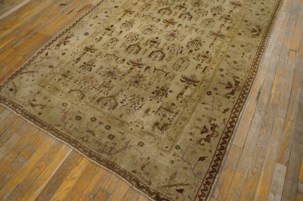 Muted gold traditional rug with brown and purple stylized motifs rests on distressed wooden floorboards.