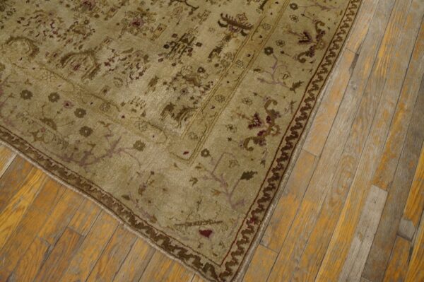 Muted traditional rug featuring beige, olive, and burgundy floral motifs rests on worn plank wood flooring.