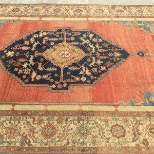Terracotta and navy rug with a bold geometric center medallion and detailed floral borders on a stone floor.